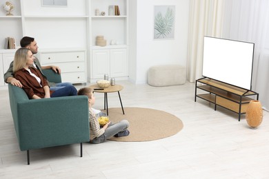 Photo of Happy family with snacks and drinks watching tv together at home