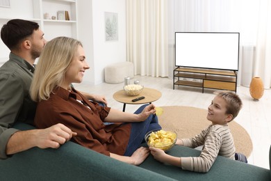 Photo of Happy family with snacks and drinks watching tv together at home