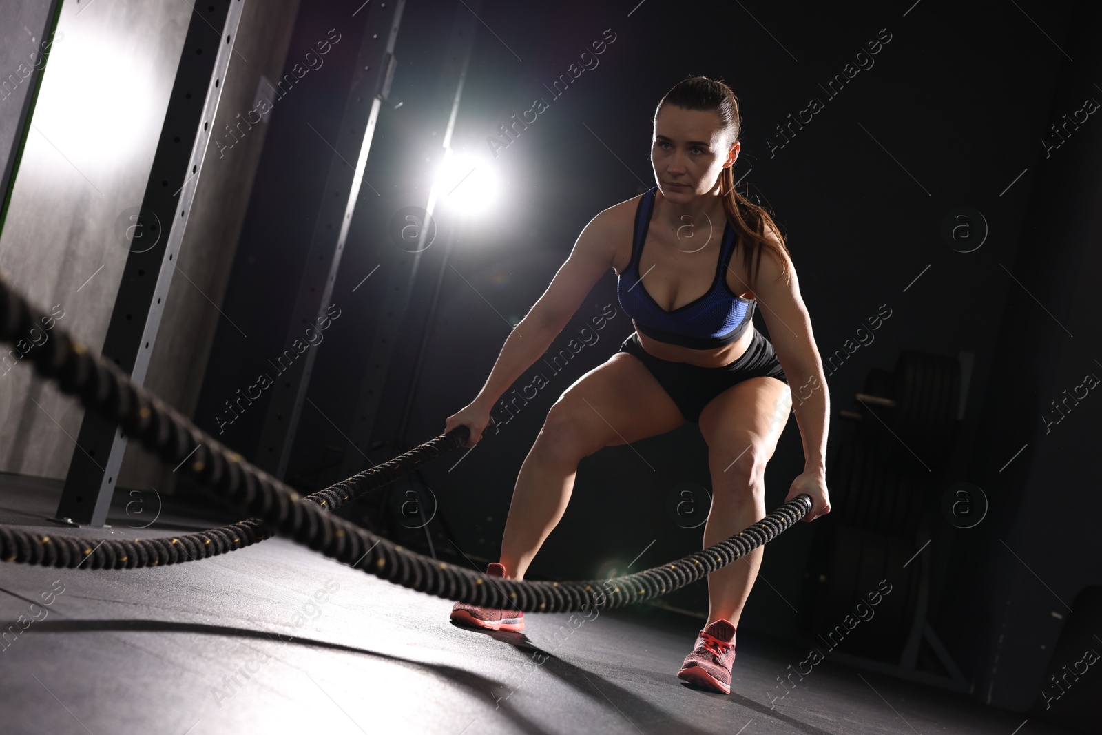 Photo of Sportswoman exercising with battle ropes during crossfit workout in gym