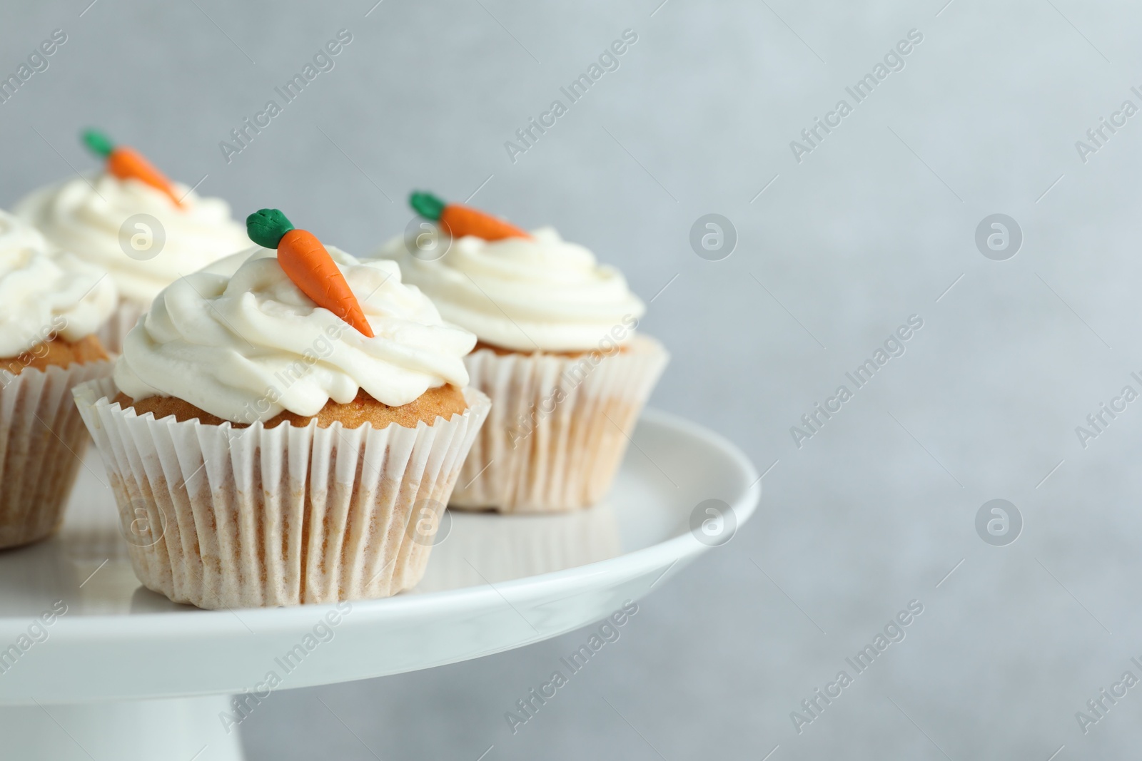 Photo of Delicious carrot cupcakes on stand against grey background, closeup. Space for text