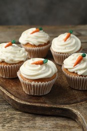 Photo of Delicious carrot cupcakes on wooden table against grey background, closeup