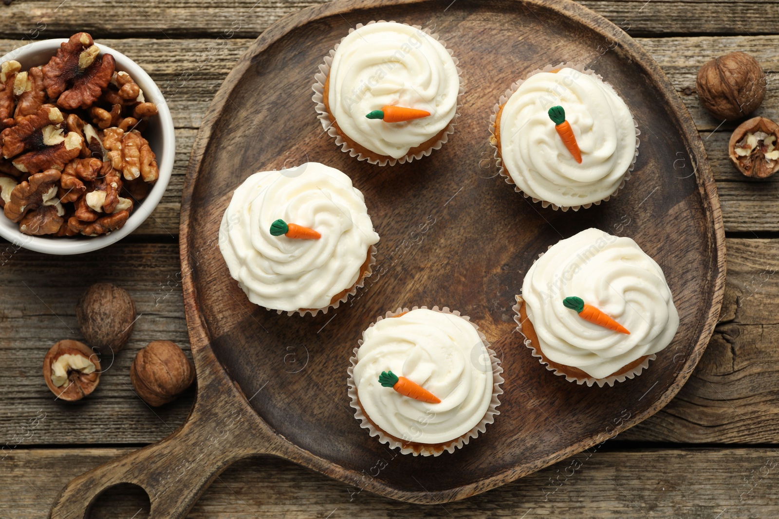 Photo of Delicious carrot cupcakes and walnuts on wooden table, flat lay