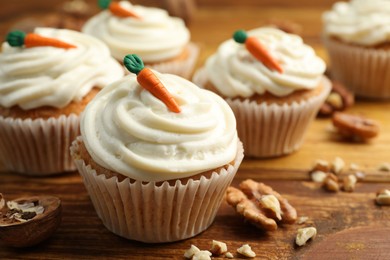 Photo of Delicious carrot cupcakes and walnuts on wooden table, closeup