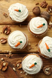 Photo of Delicious carrot cupcakes and walnuts on wooden table, flat lay