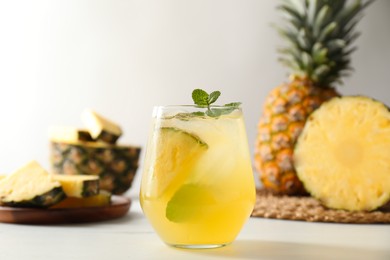 Photo of Tasty pineapple cocktail with mint in glass on light table