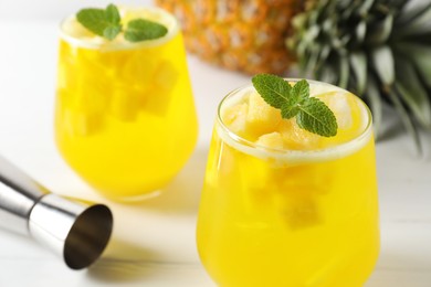 Photo of Tasty pineapple cocktail with mint in glasses and jigger on light table, closeup