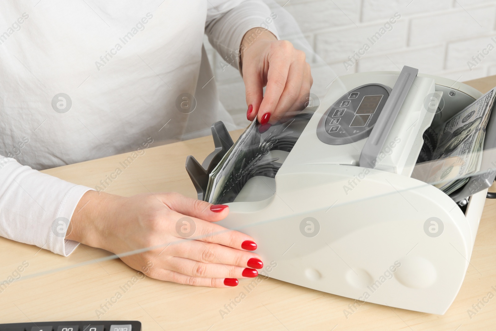 Photo of Cashier using money counting machine at table in currency exchange, closeup