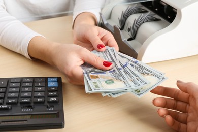 Photo of Cashier giving dollar banknotes to client at table in money exchange, closeup