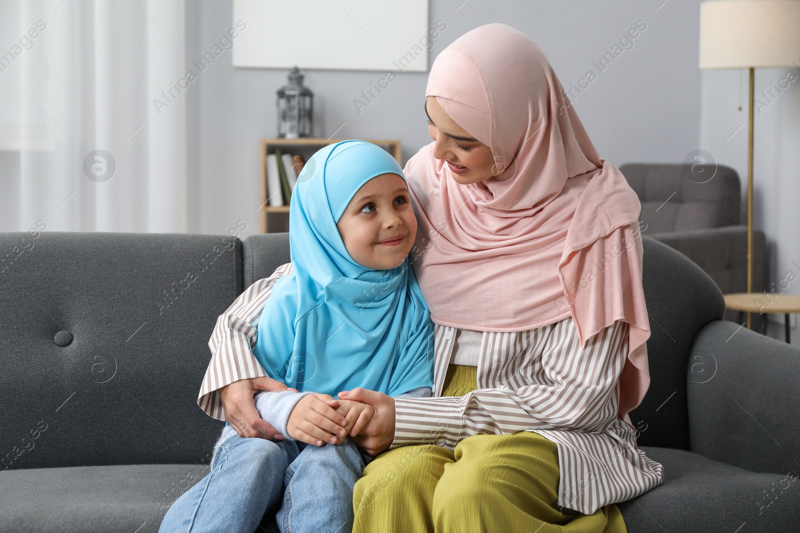 Photo of Muslim mother and her daughter sitting on sofa at home