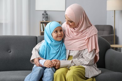 Photo of Muslim mother and her daughter sitting on sofa at home