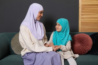 Photo of Muslim woman and her daughter sitting on sofa at home