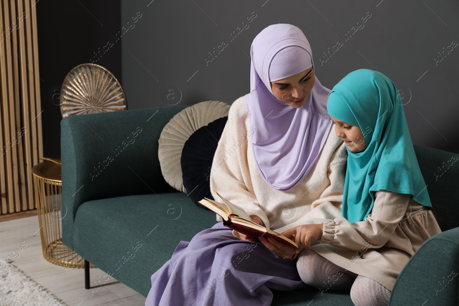 Photo of Muslim woman and her daughter reading Quran at home, space for text