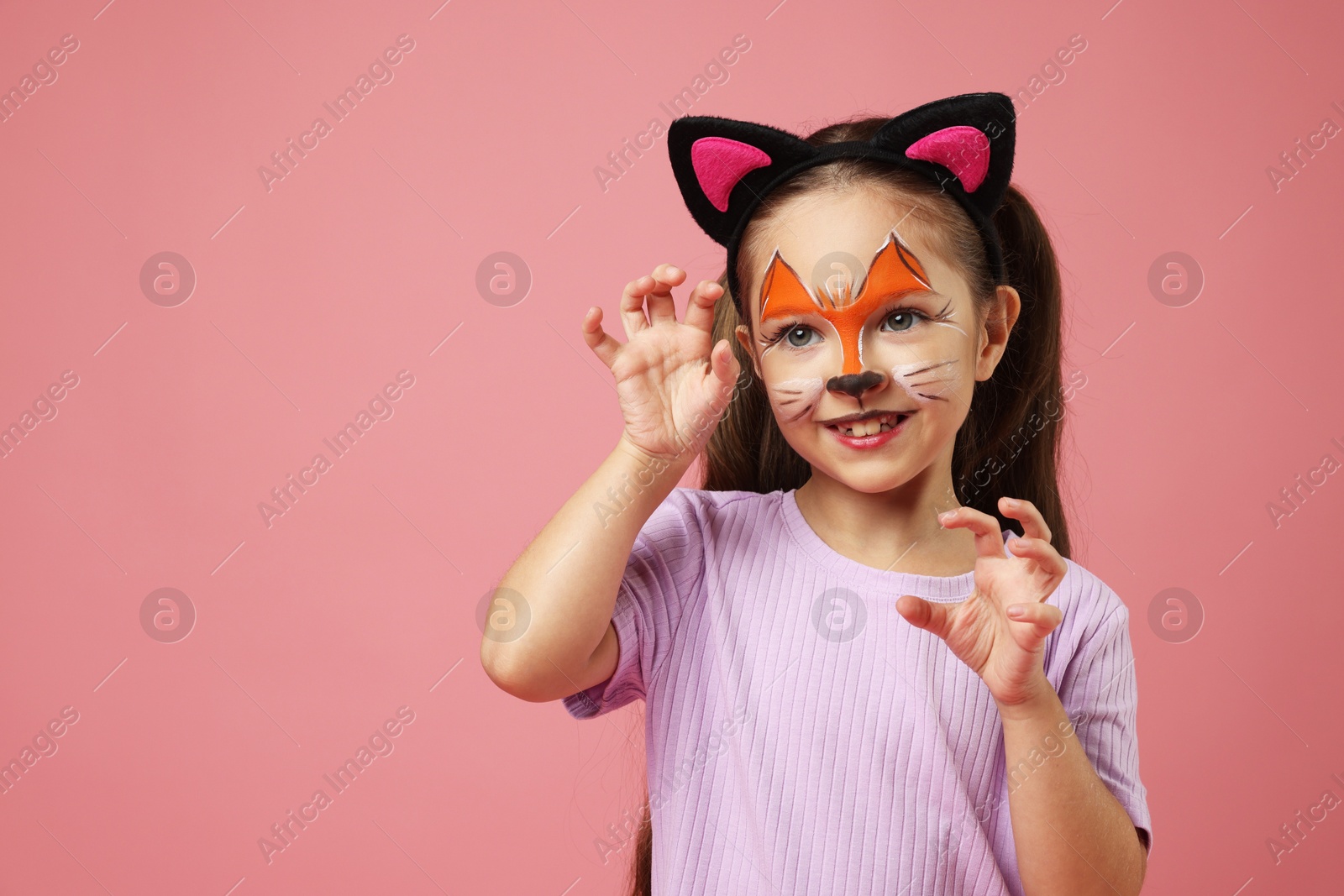 Photo of Cute girl with painted face and ears as cat on pink background, space for text