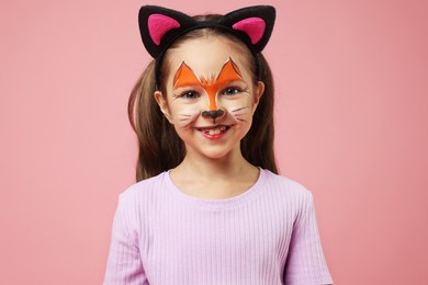 Photo of Cute girl with painted face and ears as cat on pink background