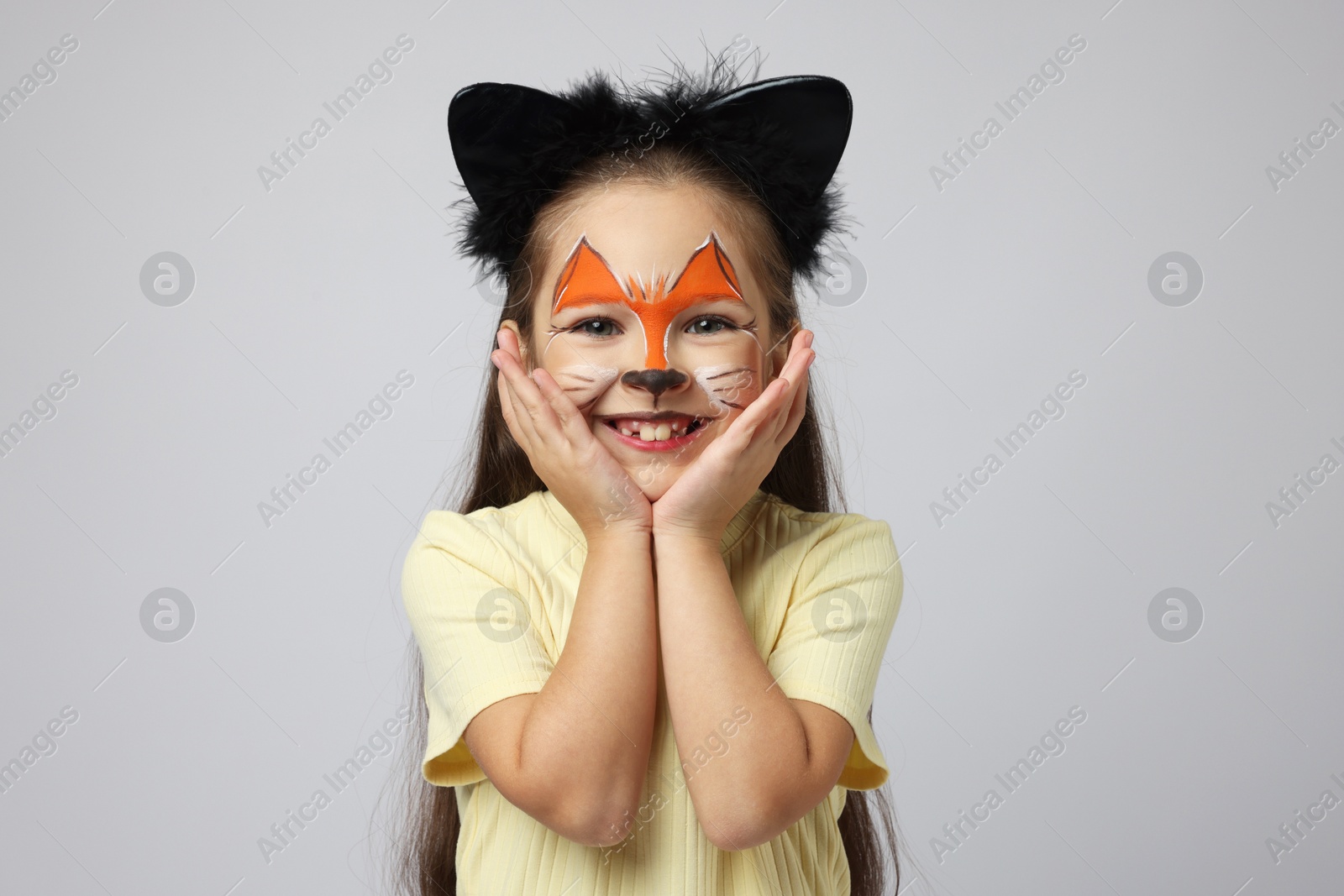 Photo of Cute girl with painted face and ears as cat on grey background