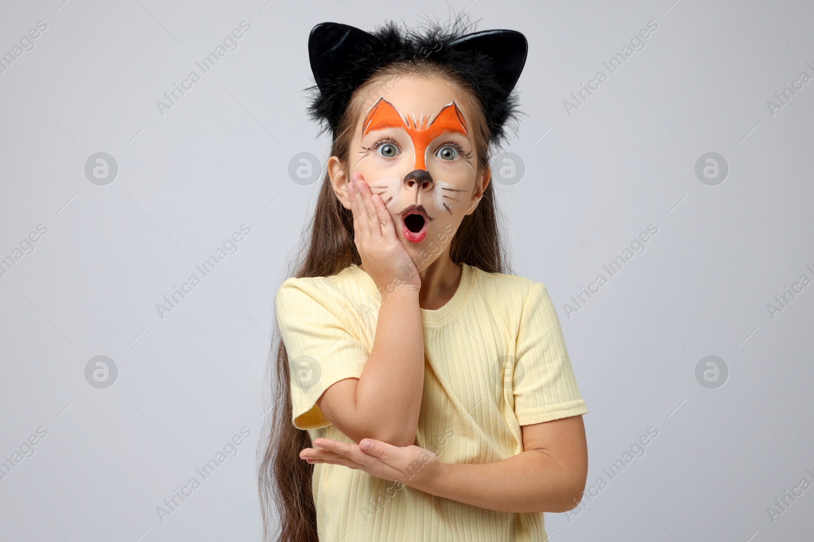 Photo of Cute girl with painted face and ears as cat on grey background