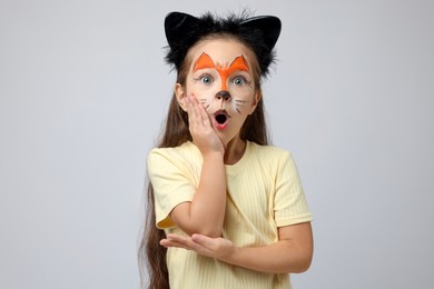 Photo of Cute girl with painted face and ears as cat on grey background