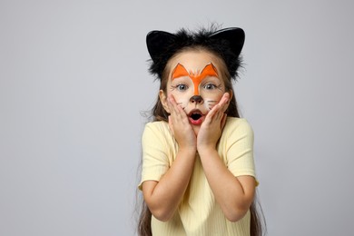 Photo of Cute girl with painted face and ears as cat on grey background, space for text