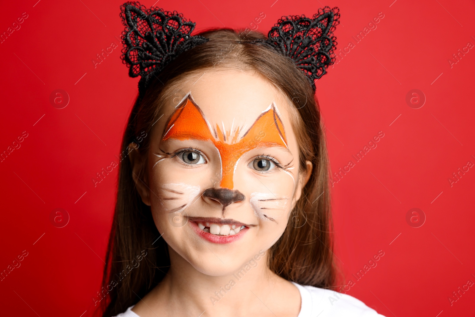 Photo of Cute girl with painted face and ears as cat on red background, closeup