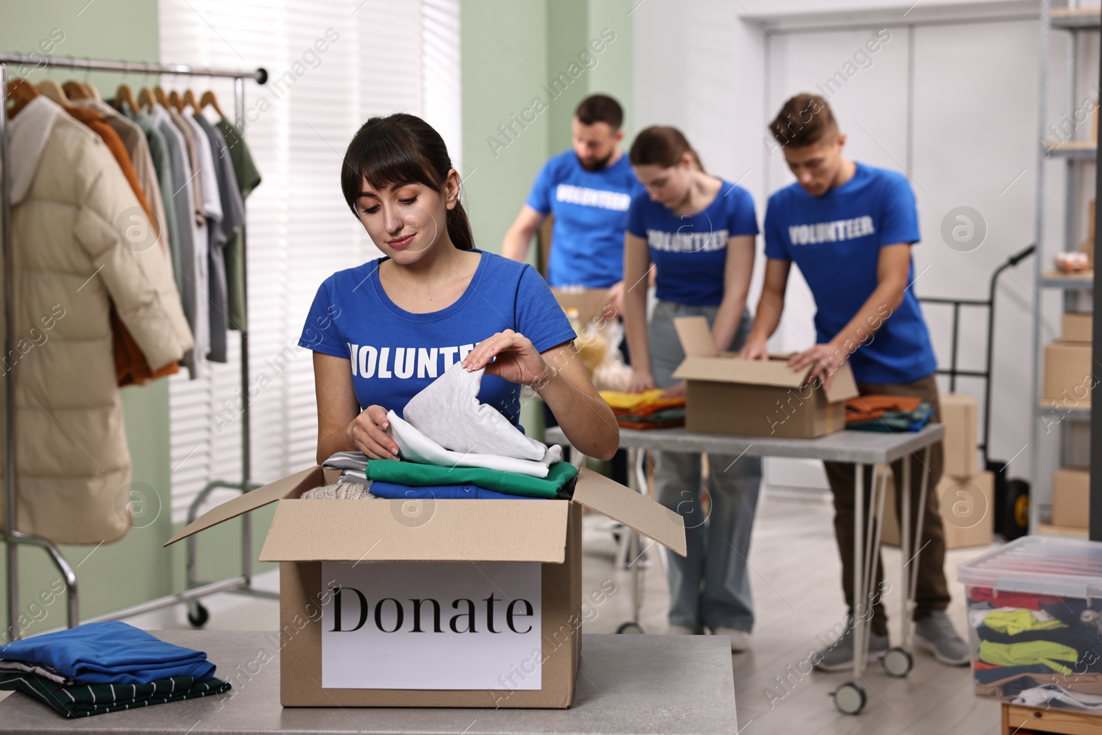 Photo of Group of volunteers packing donation goods at tables indoors, selective focus