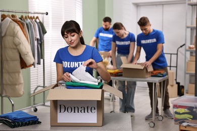 Photo of Group of volunteers packing donation goods at tables indoors, selective focus