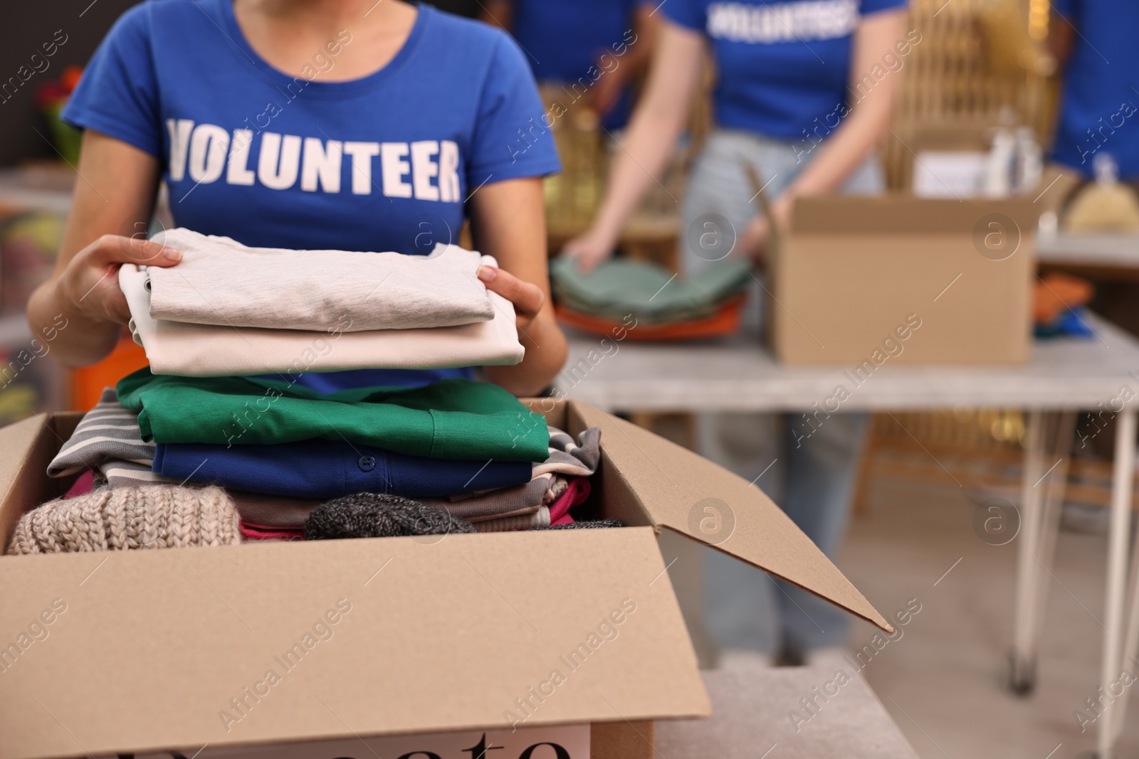 Photo of Volunteer putting clothes into donation box indoors, closeup. Space for text