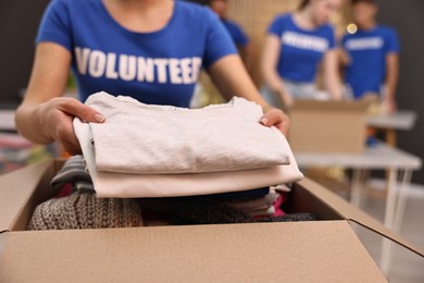 Photo of Volunteer putting clothes into donation box indoors, closeup