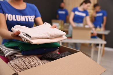 Volunteer putting clothes into donation box indoors, closeup