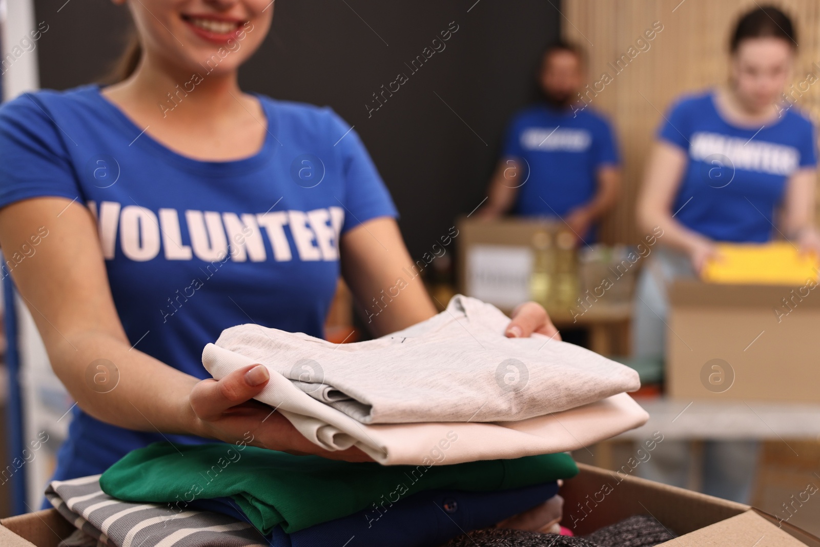 Photo of Volunteer putting clothes into donation box indoors, closeup