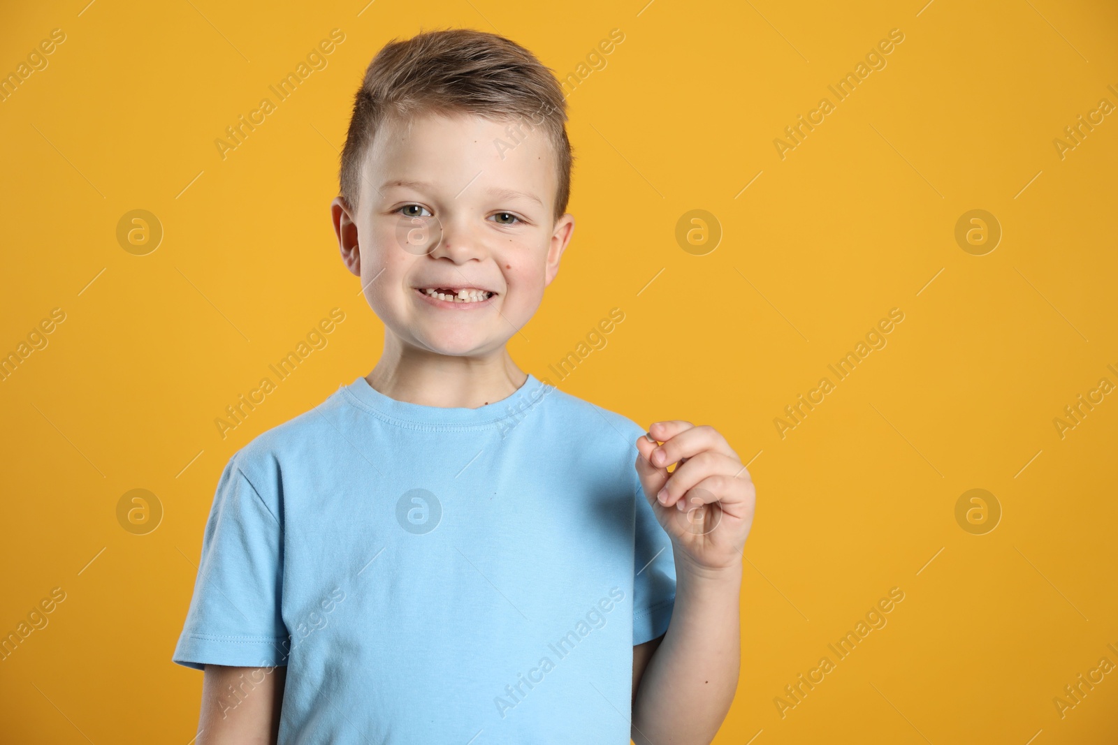 Photo of Cute little boy with missing tooth on orange background, space for text. Waiting for tooth fairy