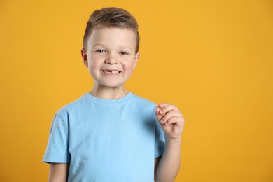 Photo of Cute little boy with missing tooth on orange background, space for text. Waiting for tooth fairy