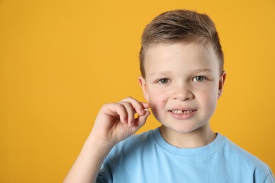 Photo of Cute little boy with missing tooth on orange background, space for text. Waiting for tooth fairy