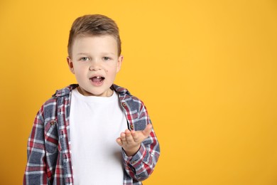 Cute little boy with missing tooth on orange background, space for text