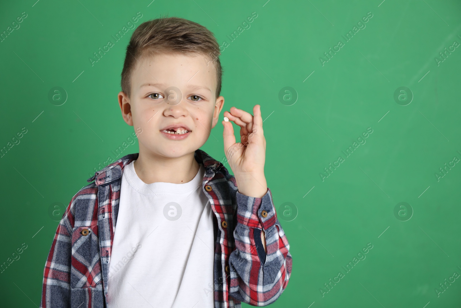 Photo of Cute little boy with missing tooth on green background, space for text. Waiting for tooth fairy