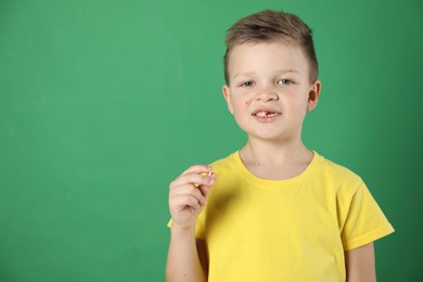 Cute little boy with missing tooth on green background, space for text. Waiting for tooth fairy