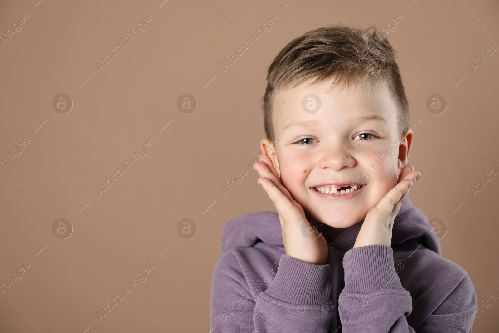 Photo of Cute little boy with missing tooth on dark beige background, space for text