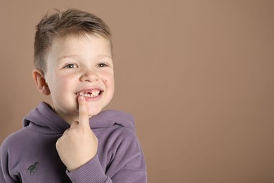 Photo of Cute little boy pointing at his missing tooth on dark beige background, space for text