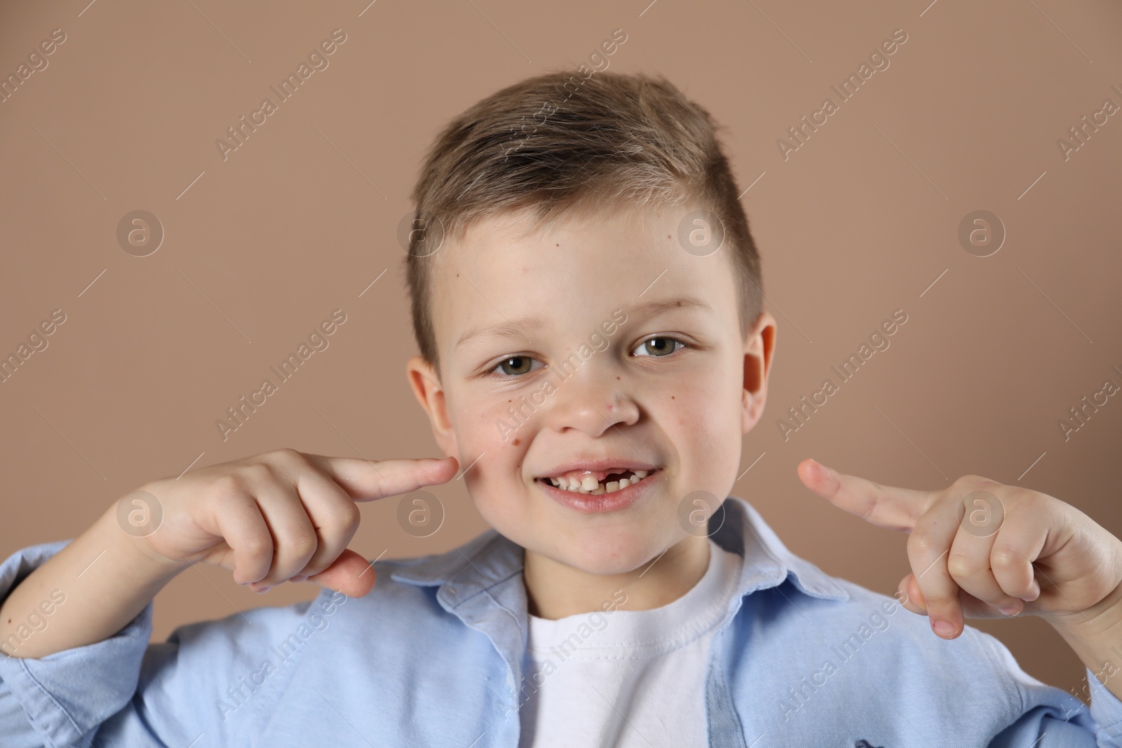 Photo of Cute little boy pointing at his missing tooth on dark beige background