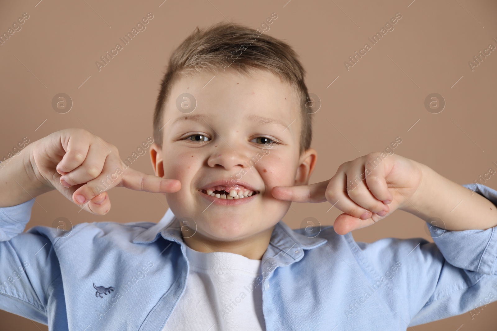 Photo of Cute little boy pointing at his missing tooth on dark beige background