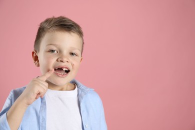 Photo of Cute little boy pointing at his missing tooth on pink background