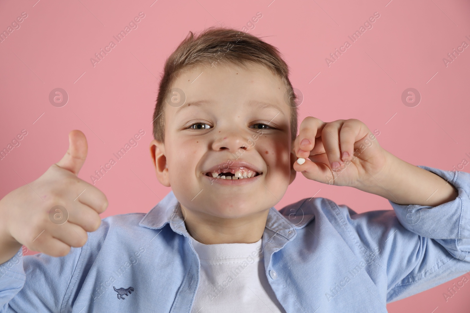 Photo of Cute little boy with missing tooth showing thumbs up on pink background. Waiting for tooth fairy