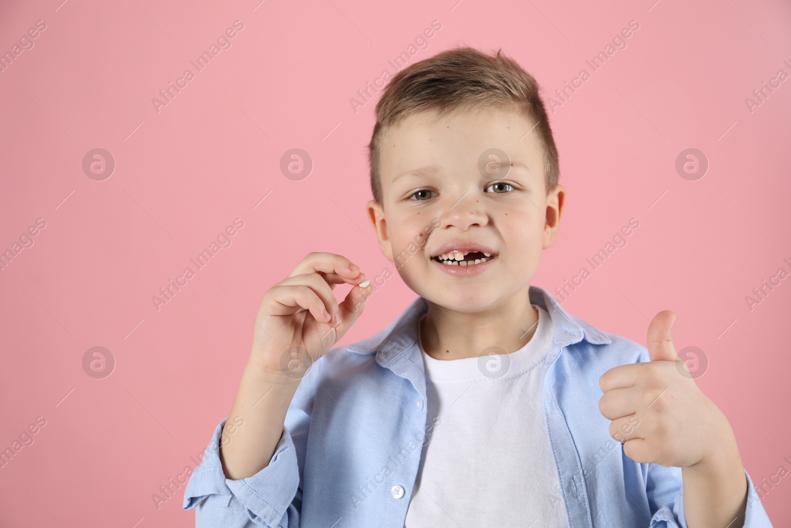 Photo of Cute little boy with missing tooth showing thumbs up on pink background, space for text. Waiting for tooth fairy