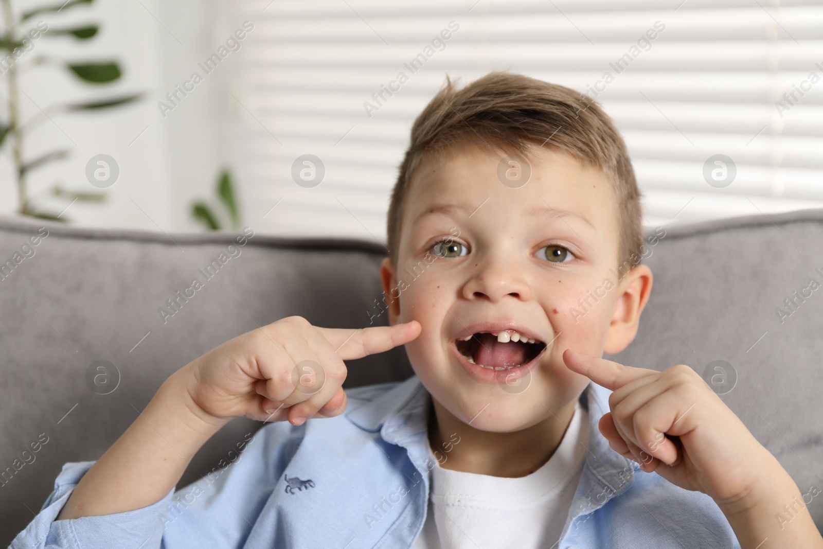 Photo of Cute little boy pointing at his missing tooth indoors