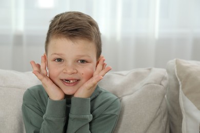 Photo of Cute little boy with missing tooth on sofa at home