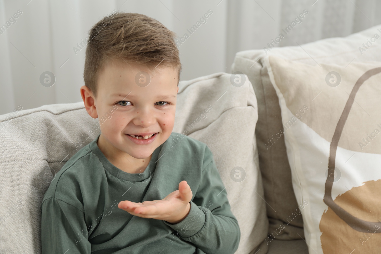 Photo of Cute little boy with missing tooth on sofa at home. Waiting for tooth fairy