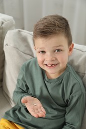 Photo of Cute little boy with missing tooth on sofa at home. Waiting for tooth fairy