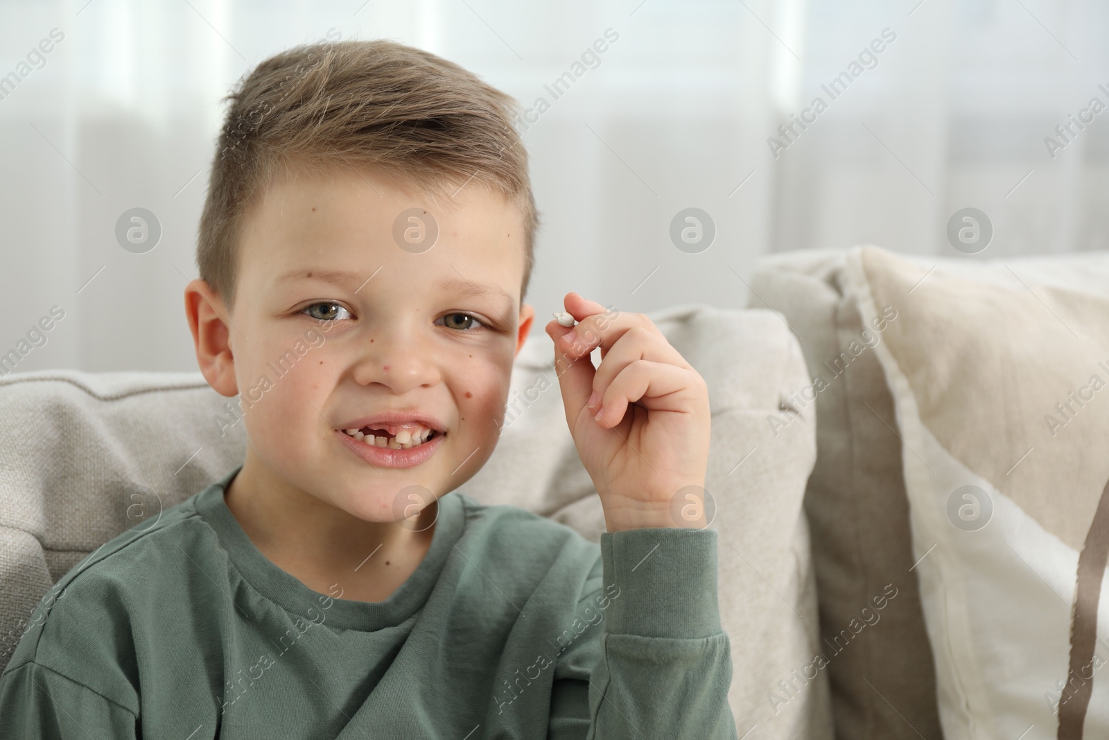 Photo of Cute little boy with missing tooth on sofa at home. Waiting for tooth fairy