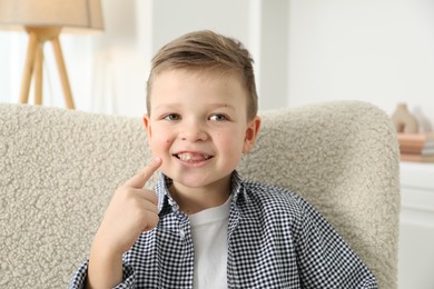 Photo of Cute little boy pointing at his missing tooth indoors