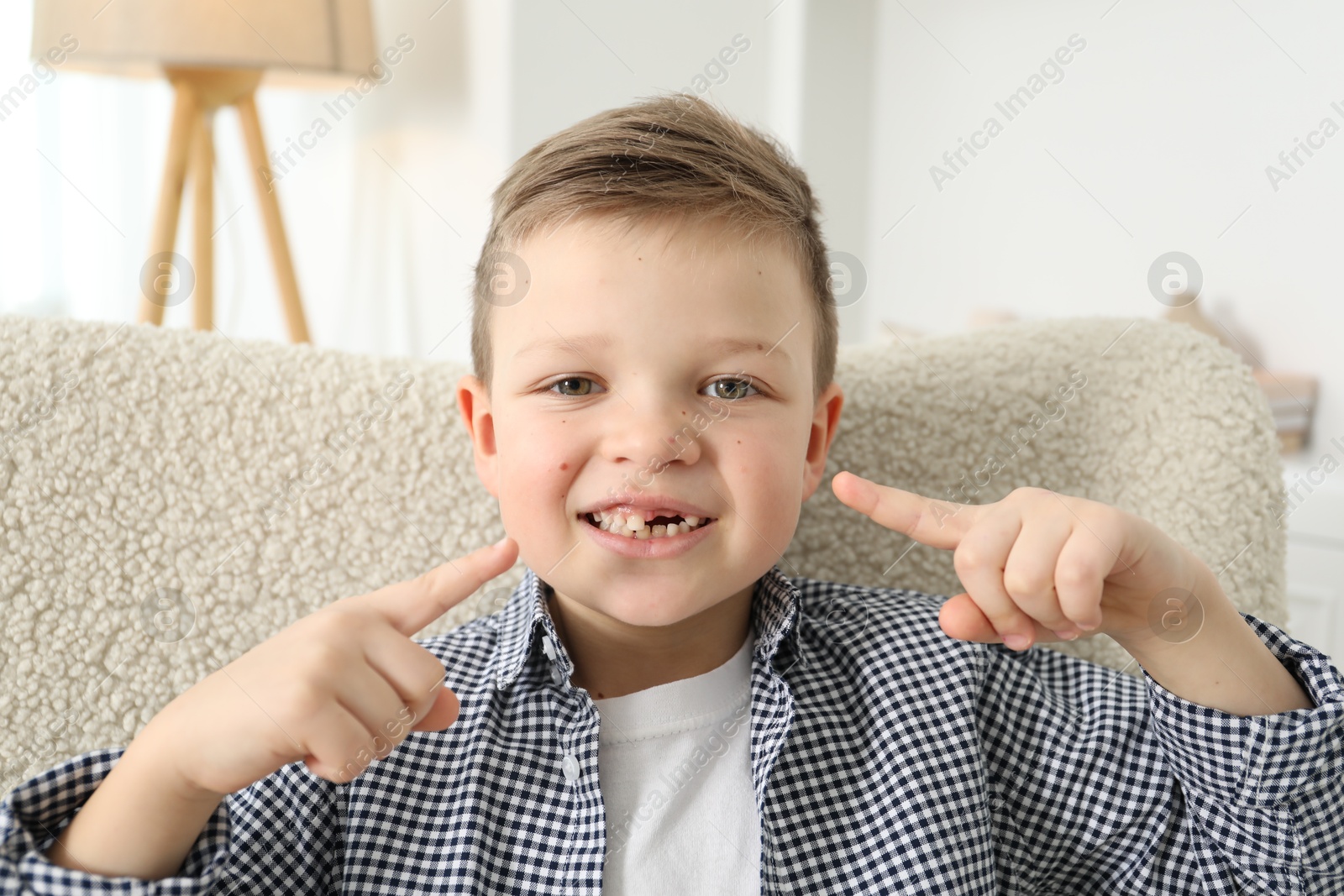 Photo of Cute little boy pointing at his missing tooth indoors