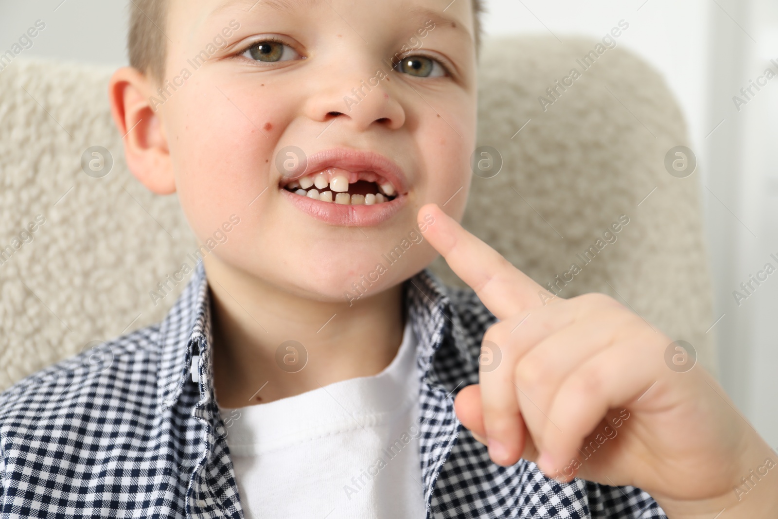 Photo of Cute little boy pointing at his missing tooth indoors, closeup